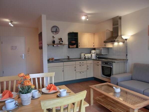 A compact kitchen with a stove, microwave, and cabinets. There is a dining table with chairs and a small coffee table.