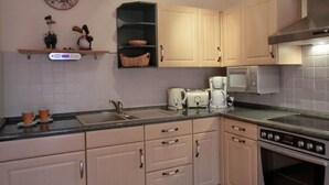 Een keuken met lichte kastjes, een spoelbak, een broodrooster, een magnetron en een fornuis.