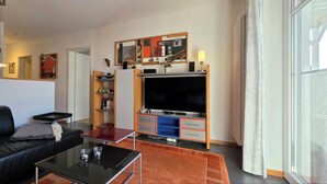 Un salon moderne avec un canapé en cuir noir, une table basse en verre et un téléviseur à écran plat posé sur un meuble en bois.