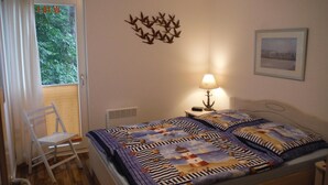 Een slaapkamer met een bed, een stoel, een nachtkastje met een lamp, een decoratie aan de muur, en een raam met gordijnen.