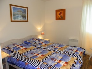 Een slaapkamer met een bed overdekt met een quilt met een nautisch thema, een nachtkastje met een lamp en twee ingelijste foto’s aan de muur.