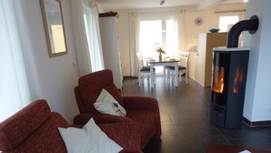 Een woonkamer met een rode bank, witte kussens, een houten salontafel en een open haard.