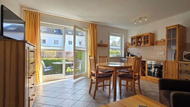Une cuisine moderne avec des meubles en bois, un coin repas comprenant une table et des chaises, et un téléviseur posé sur un meuble.