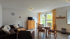 Un salon comprenant un canapé, une table basse, un meuble en bois, un téléviseur, une table à manger avec des chaises et une fenêtre avec des rideaux.