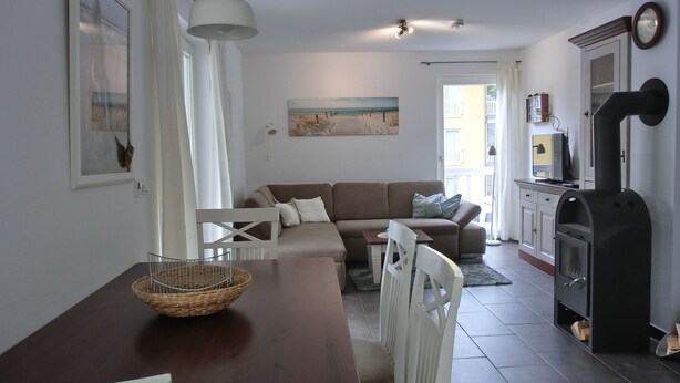 Een moderne woonkamer met een houten eettafel, witte stoelen, een bruine bank en een zwart houtkachel.