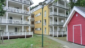 Een meerlaags woongebouw met balkons, een rode garage en een geplaveid binnenterrein.