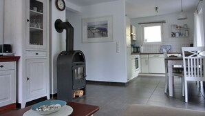 Een moderne keuken met witte kasten, een ingebouwde oven, een magnetron en een kookplaat. Er is een eethoek met een tafel en stoelen, en een klok aan de muur.