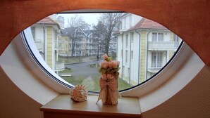 A view from a window with a triangular skylight, overlooking a residential area with multi-story buildings and a street. - 3-zimmer-fewo im 1. OG mit Balkon mit 2 Schlafzimmern für 4 Personen, Wlan (Graal-Müritz)