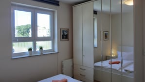 A bedroom with a large wardrobe, a window with a view, and a bedside table with a lamp. - 3-zimmer-fewo im 1. OG mit Balkon mit 2 Schlafzimmern für 4 Personen, Wlan (Graal-Müritz)