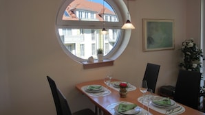 A dining area with a round window, a table set for two, and a view of buildings outside. - 3-zimmer-fewo im 1. OG mit Balkon mit 2 Schlafzimmern für 4 Personen, Wlan (Graal-Müritz)