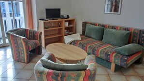 Una sala de estar con un sofá, dos sillones, una mesa de centro, un televisor y una estantería.