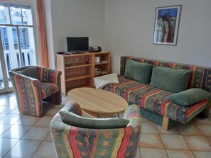 A living room with a sofa, two armchairs, a coffee table, a TV, and a bookshelf.