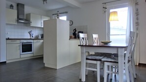 Een moderne keuken met witte kastjes, een ingebouwde oven en een eethoek met een tafel en stoelen.