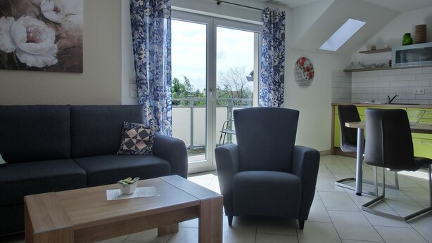 Una sala de estar con un sofá, una mesa de centro y una silla. Hay un balcón con vistas al exterior.