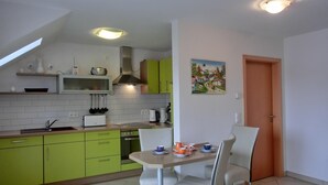 Una cocina con armarios verdes, una encimera blanca y una zona de comedor con mesa y sillas.