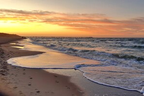 A beach with waves at sunset, a pier in the distance, and footprints on the sand. - Strandnahes 2-zimmer-fewo im 1.og, Balkon und Wlan (Graal-Müritz)