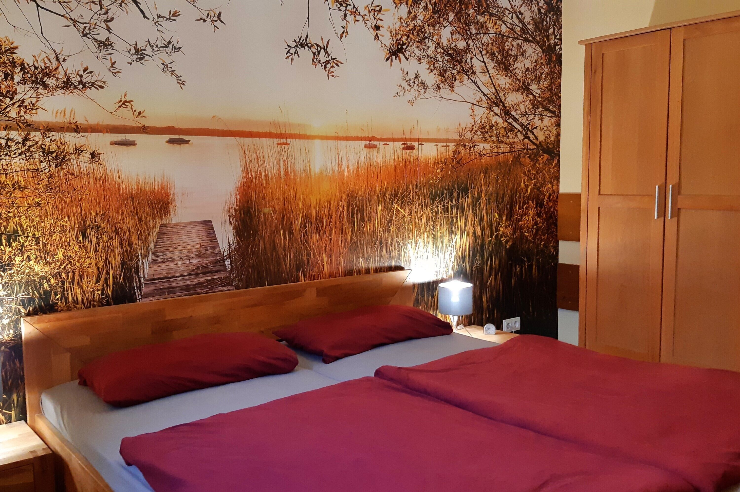 Una camera da letto con testiera in legno, un letto con lenzuola rosse, un comodino con una lampada e un armadio.