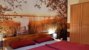 Ein Schlafzimmer mit hölzernem Kopfteil, einem Bett mit roter Bettwäsche, einem Nachttisch mit Lampe und einem Kleiderschrank.