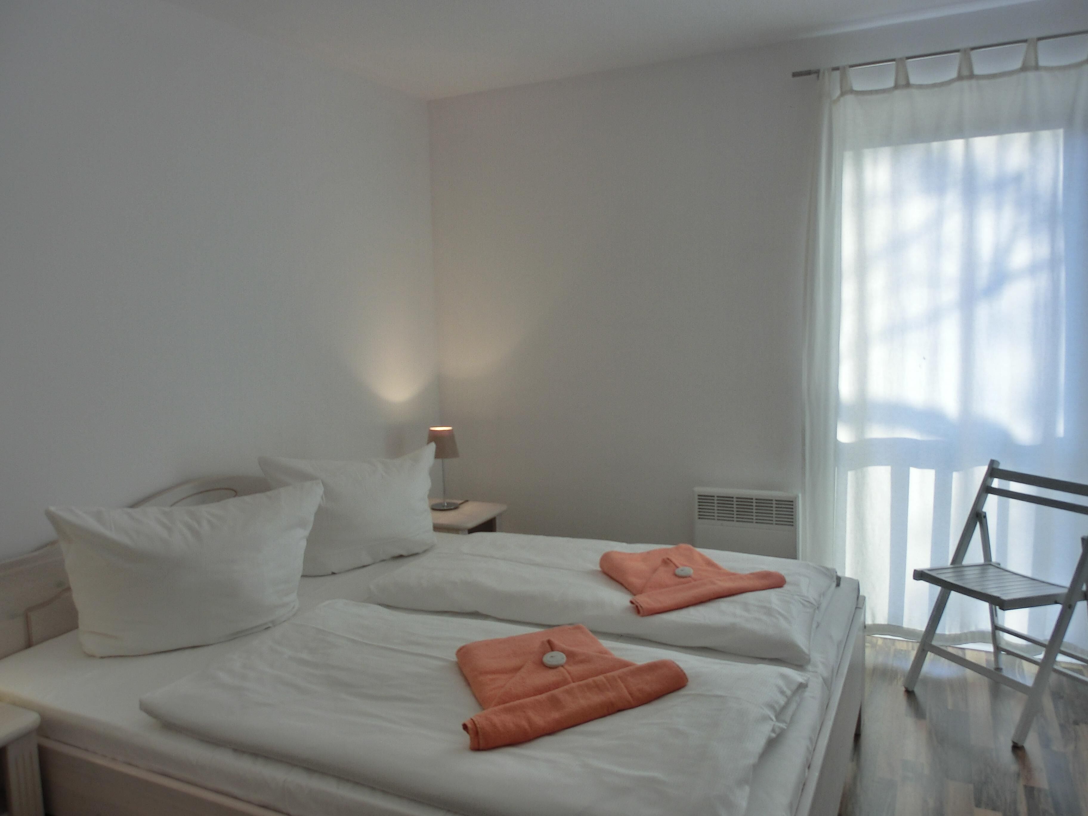 Une chambre d’hôtel avec deux lits, une table de chevet, une lampe, une chaise et une fenêtre avec des rideaux.