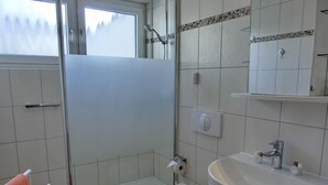 Un baño con ducha, inodoro, lavamanos y un perchero con toalla.