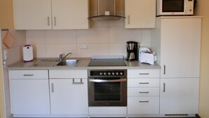 Cocina compacta con armarios blancos, un lavamanos de acero inoxidable, microondas, cafetera, tostadora y horno.