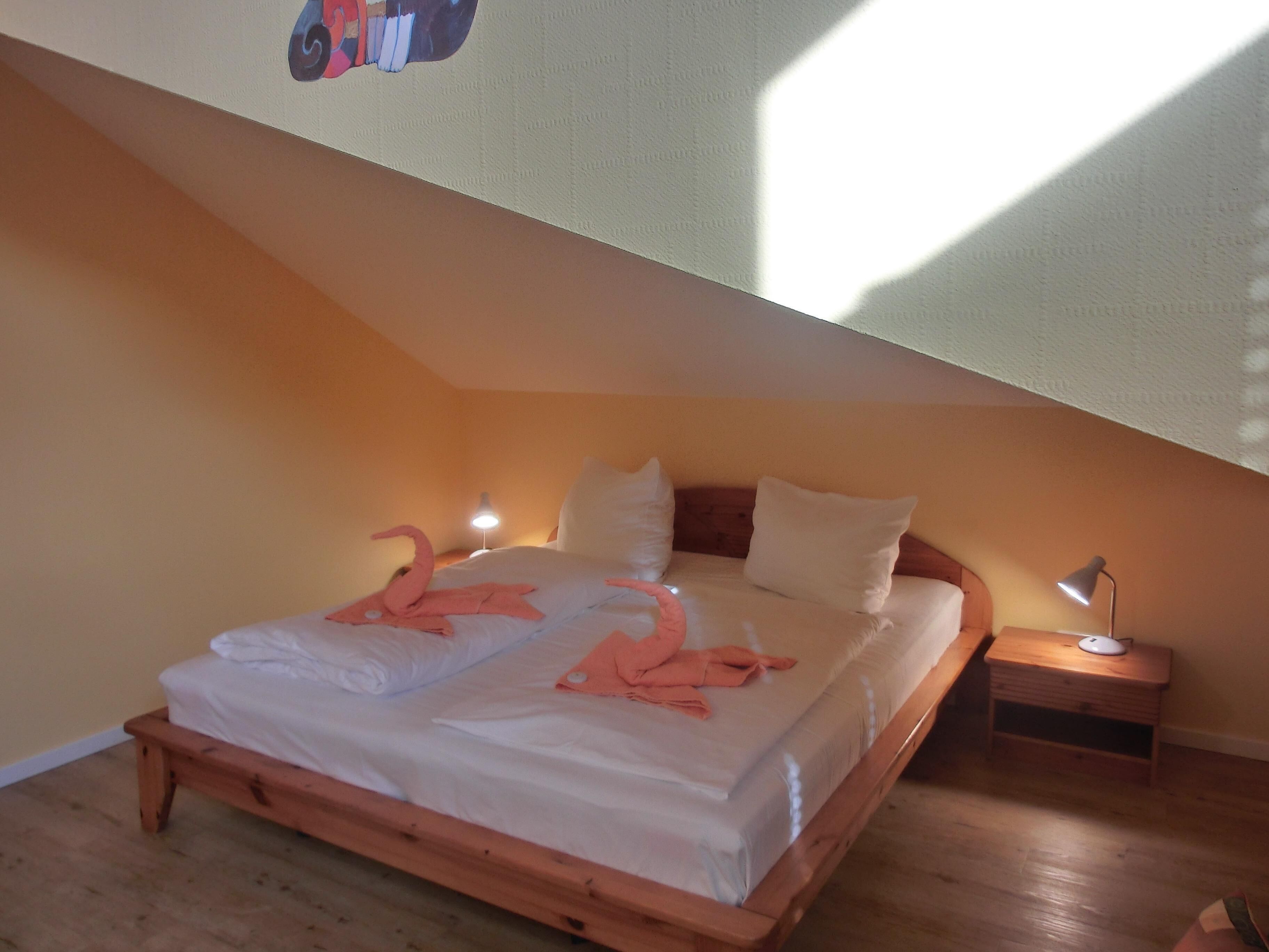 A bedroom with a wooden bed, white bedding, a pink flamingo decoration, two bedside lamps, and a wooden nightstand.
