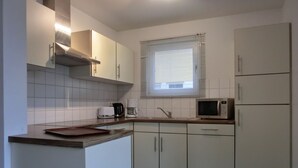 A modern kitchen with white cabinets, a microwave, a coffee maker, and a window with blinds. - 4-zi-fewo für 6 Pers.im 2.og, Wlan, Strandnah (Graal-Müritz)