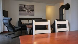 A living room with a wooden table, a black sofa, a white armchair, and a black chair. There is a painting on the wall and a black heater on the right. - 4-zi-fewo für 6 Pers.im 2.og, Wlan, Strandnah (Graal-Müritz)
