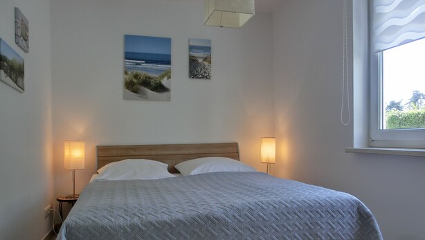 Een net opgemaakt bed met een houten hoofdbord, twee bedlampen en drie ingelijste foto's aan de muur.