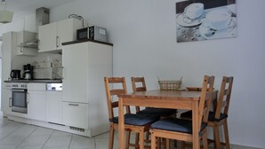 Een compacte keuken met witte kastjes, een kookplaat en een magnetron. Er staat een eettafel met houten stoelen en een mand op de tafel.