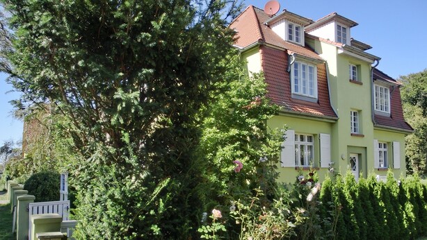 A two-story house with a red-tiled roof, surrounded by lush greenery and a well-maintained garden. - Ferienappartement für bis 2 Pers. in Unmittelbarer Strandnähe (Graal-Müritz)