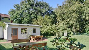 A small, single-story building with a wooden door and windows, surrounded by a grassy area and trees. - Ferienappartement für bis 2 Pers. in Unmittelbarer Strandnähe (Graal-Müritz)