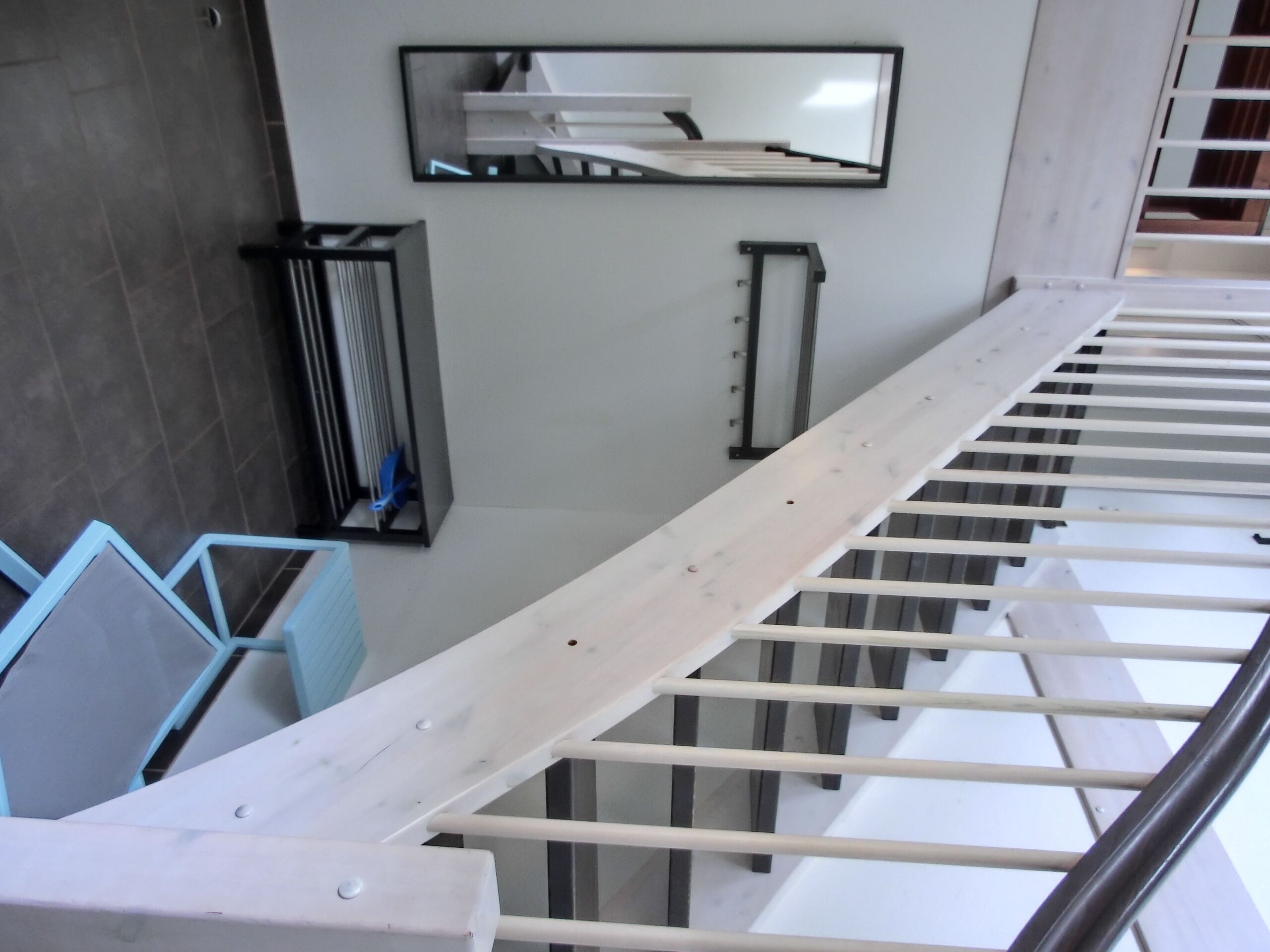 Un escalier avec des rampes et une main courante en métal, menant à un palier agrémenté d’un miroir et d’un radiateur.