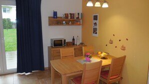 Un comedor con una mesa de madera, sillas, un microondas y un estante pequeño con libros y objetos decorativos.