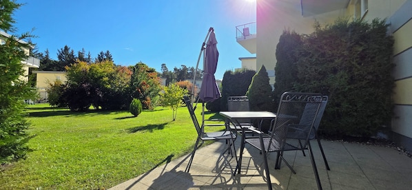 An outdoor patio area with a table and chairs, surrounded by a well-maintained lawn and trees.