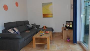 Ein Wohnzimmer mit einer Couch, einem Couchtisch und einem Fernseher auf einem Holzständer.