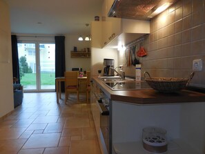 Une cuisine moderne dotée d’un grand îlot central, d’un coin repas avec une table et des chaises, et offrant une vue sur l’extérieur grâce à une porte coulissante.