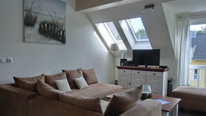 Ein Wohnzimmer mit braunem Sofa, einem Flachbildfernseher auf einem Holzboden und einem Oberlicht.
