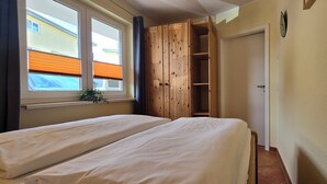 Ein Schlafzimmer mit zwei Betten, einem Holzschrank, einem Fenster mit Jalousien und einer Tür.