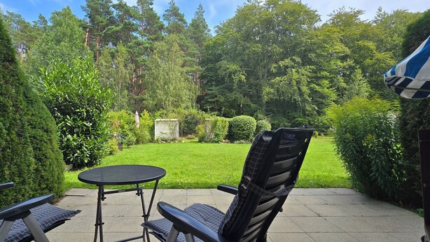 Eine Terrasse mit zwei Stühlen und einem kleinen runden Tisch, umgeben von üppiger Bepflanzung und einem gepflegten Rasen.