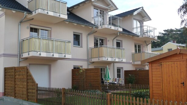 Ein mehrgeschossiges Wohnhaus mit Balkonen, einem Holzzaun und einer kleinen Holzkonstruktion.