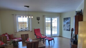 Ein geräumiges Wohnzimmer mit Essbereich, großen Fenstern und einem roten Sessel.