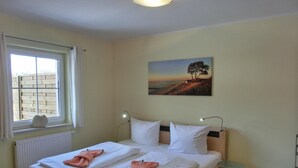 Ein Doppelbett mit weißen Leinentüchern und pinkfarbenen Handtüchern, ein Fenster mit Blick auf einen Holenzaun und ein Baumgemälde an der Wand.