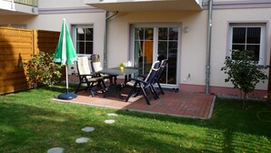 Eine Terrasse mit Tisch, Stühlen und einem kleinen Tisch mit Blumen in einer Vase.