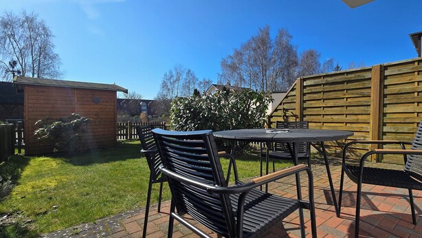Eine Terrasse im Freien mit Tisch und Stühlen, einem Holzzaun und einer Rasenfläche.