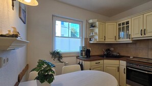 Eine Küche mit weißen Schränken, einem Backofen, einer Kaffeemaschine und einem Fenster mit Jalousien.