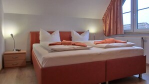 A neatly made bed with white and orange bedding, a bedside lamp, and a nightstand with a drawer. - 3-zi.-fewo mit 2 Schlafzimmern + Kostenfreien W-lan-zugang (Graal-Müritz)