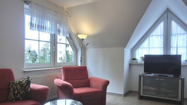 A living room with a red sofa, a glass coffee table, a TV on a cabinet, and large windows with curtains. - 3-zi.-fewo mit 2 Schlafzimmern + Kostenfreien W-lan-zugang (Graal-Müritz)
