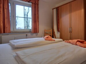 A bedroom with two beds, a window, and wooden wardrobe.