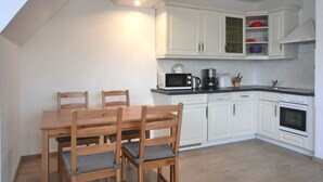 A kitchen with white cabinets, a wooden dining table with chairs, a microwave, a coffee maker, and a stove. - 3-zi.-fewo mit 2 Schlafzimmern + Kostenfreien W-lan-zugang (Graal-Müritz)